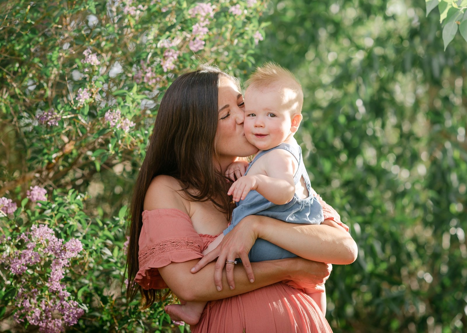 Baby boy looking at camera while mom is kissing him during a family photoshoot in Colorado