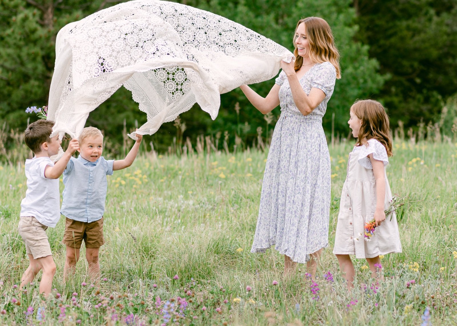 A candid photo of a mother and her kids playing with a blanket in a meadow of wildflowers in Nederland Colorado