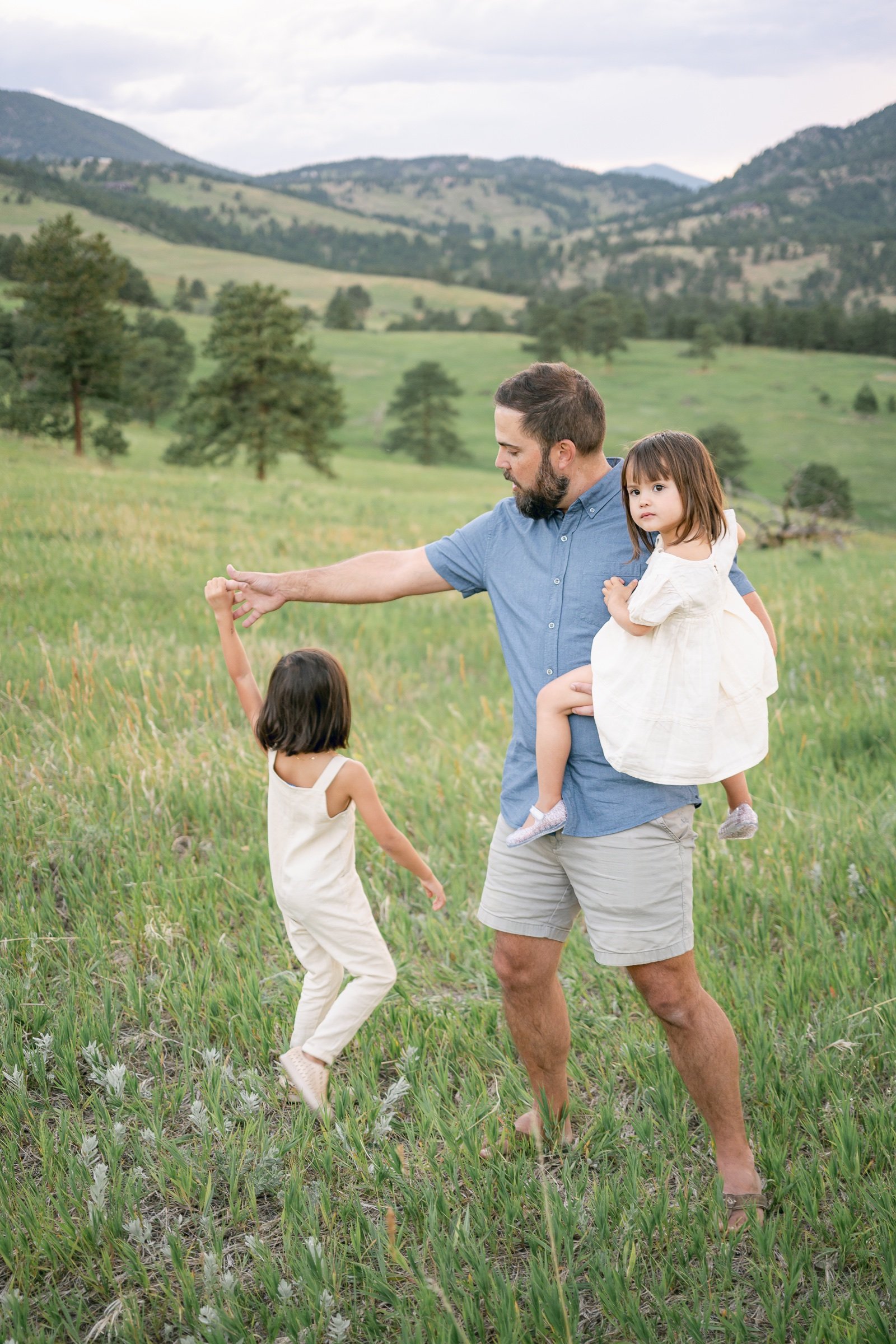 Father dancing with his daughters in a lush green mountain meadow at sunset in Golden Colorado