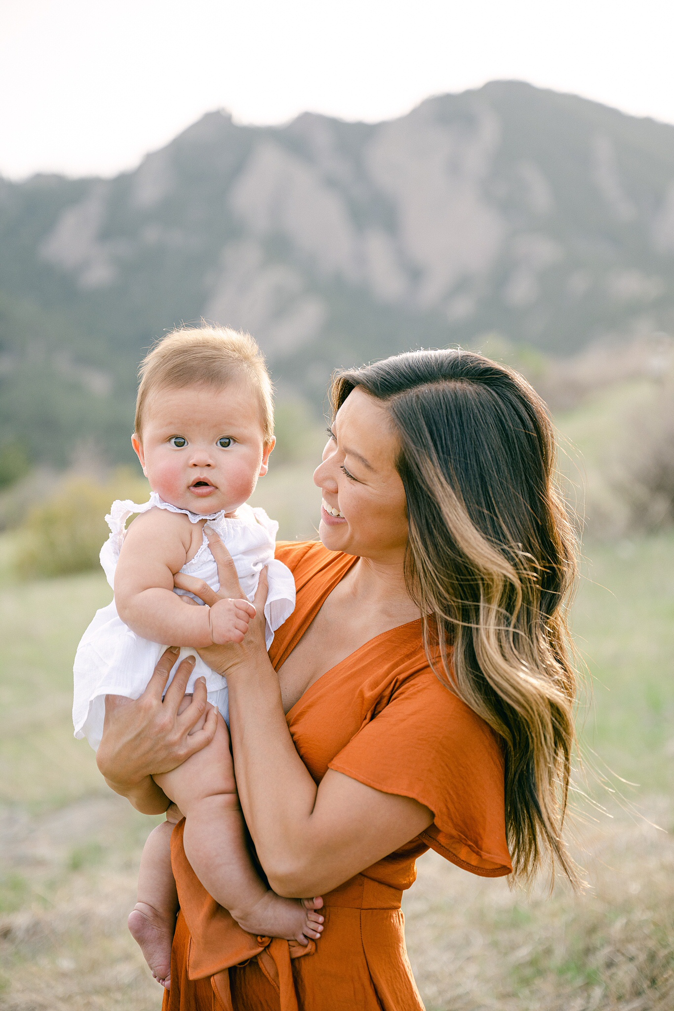 A young mother wearing a orange dress holding her six month baby during a portrait session in Boulder, Colorado.