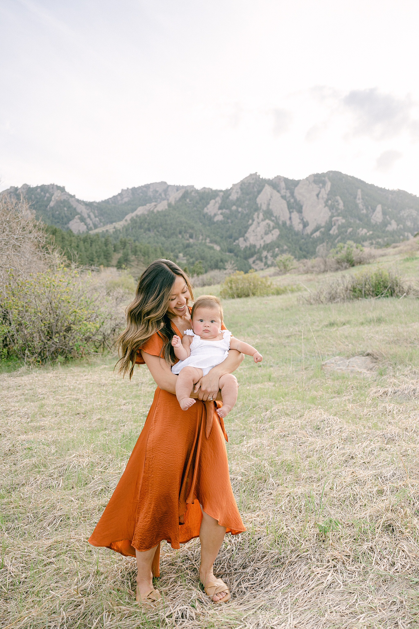 A young mother holding her six month baby during a photo session in Boulder, Colorado with mountains in the background.