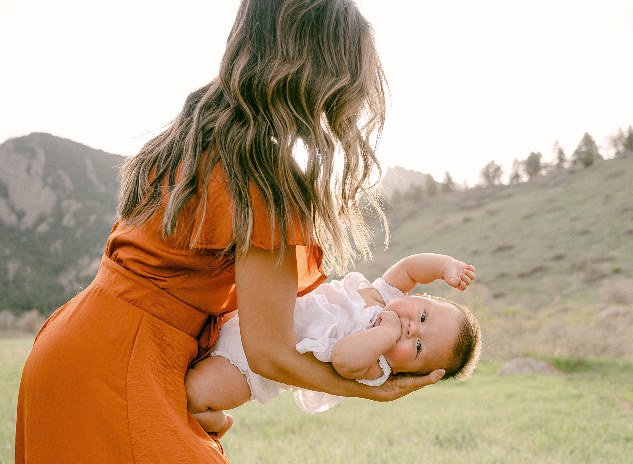 A six month baby waving during a photo session in Boulder, Colorado with mountains in the background.