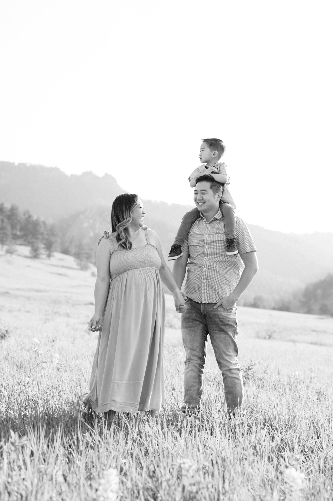 Black and white photo of a family of three laughing while having their photos taken in Chautauqua Park in Boulder, Colorado with mountains in the background