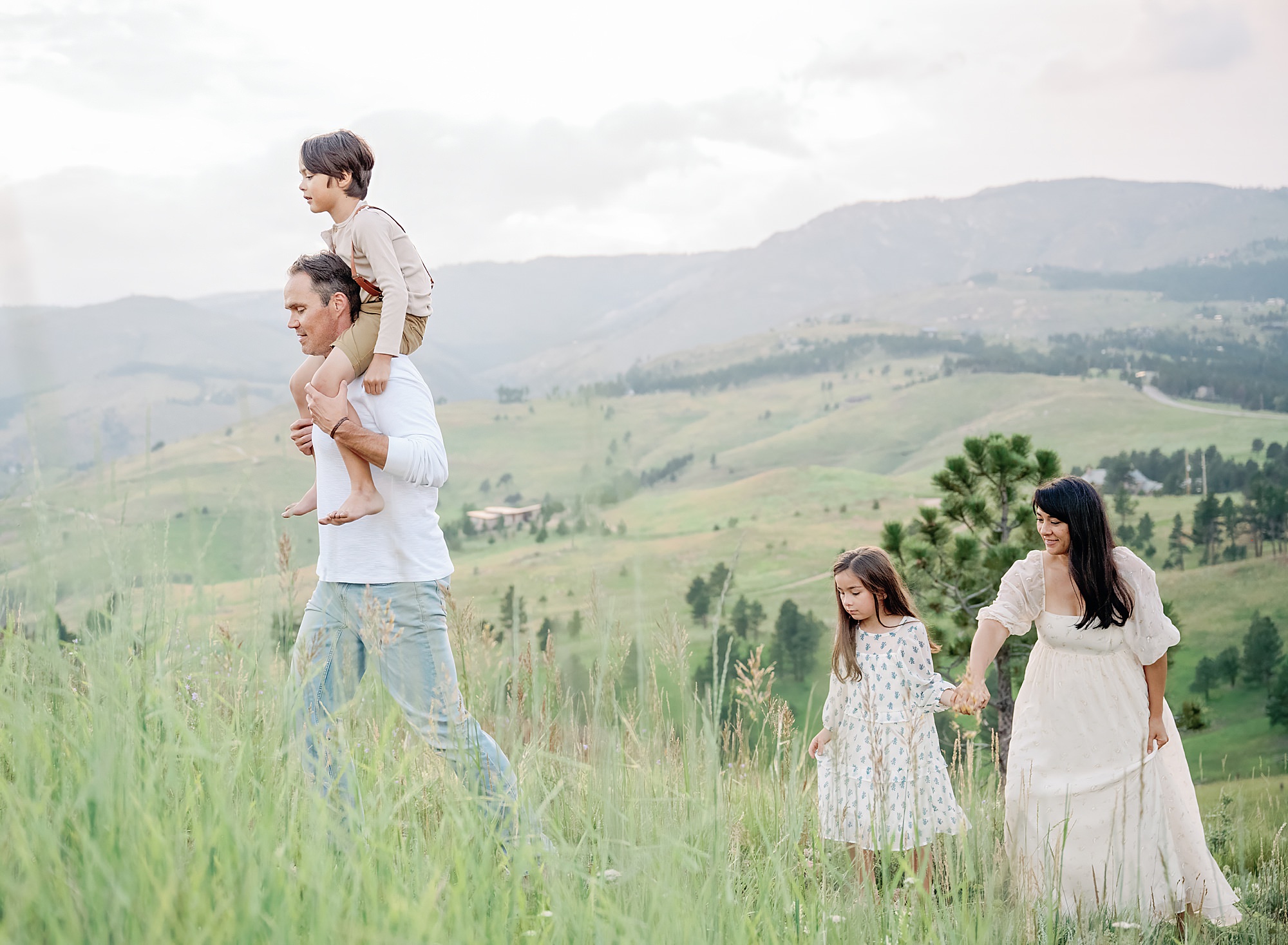 Photograph of a young family from Denver walking in a field with mountains in the background taken a family photographer in Boulder Colorado