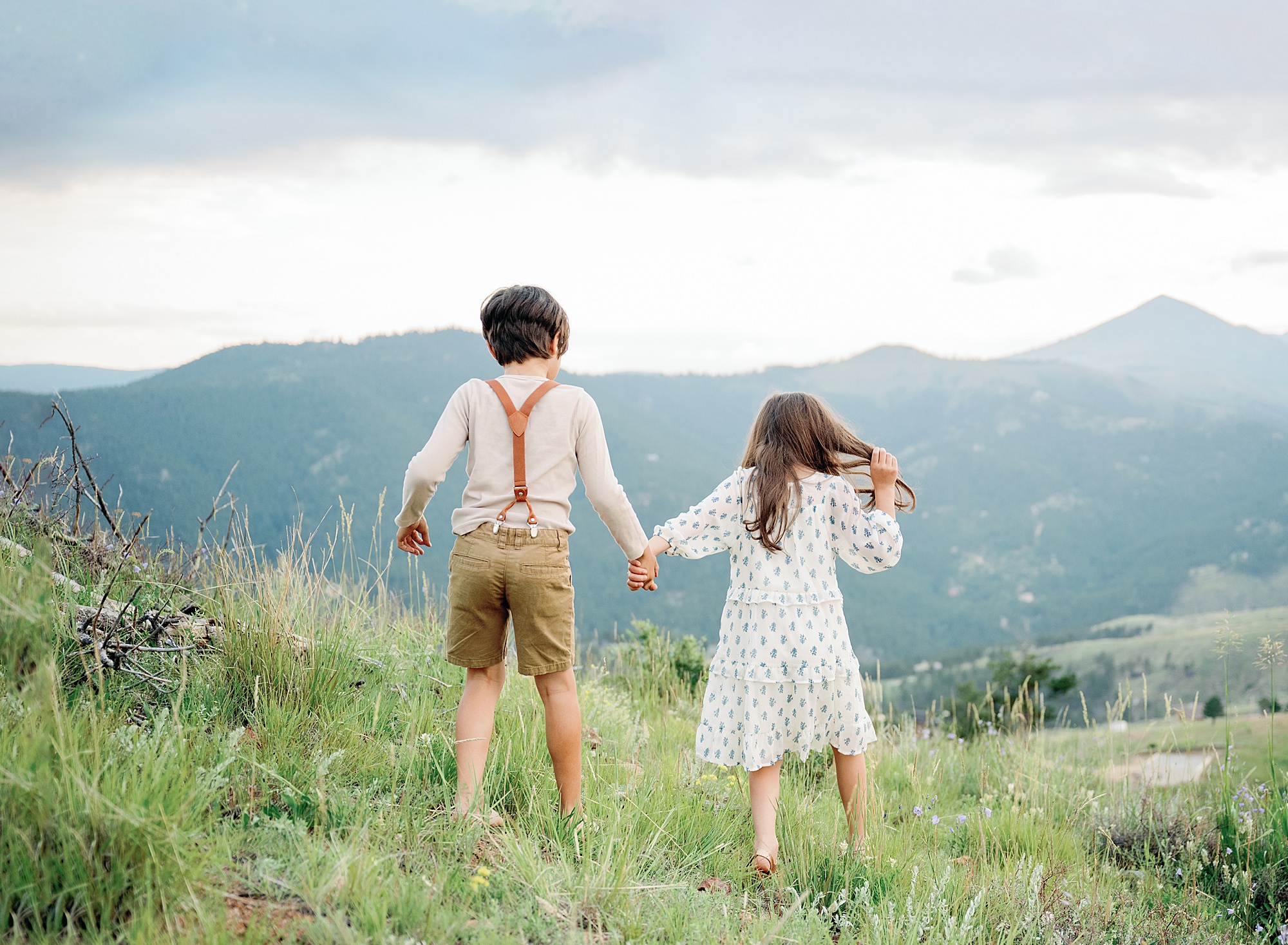 A portrait of a young Denver boy and his sister holding hands walking with the mountains in the background taken a family photographer in Boulder Colorado